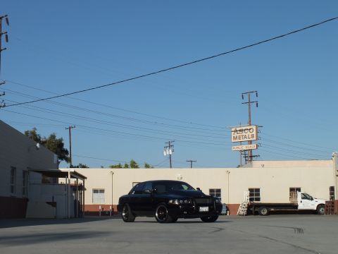 2003 Ford Crown Victoria - black Ford Crown Victoria sits in a sunlit industrial lot with an Asco Metals public scale sign and a flatbed truck behind it.