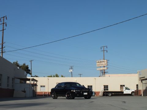 2003 Ford Crown Victoria - black Ford Crown Victoria sits centered in a wide industrial parking lot beneath power lines and an Asco Metals sign.