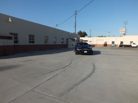 2003 Ford Crown Victoria - black sedan with a push bar sits beside a warehouse as curved tire skid marks streak across the concrete lot.