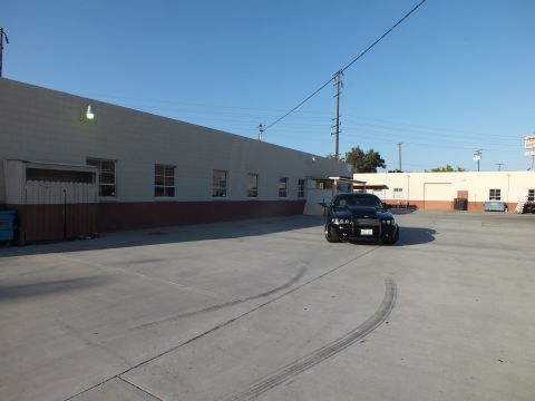 2003 Ford Crown Victoria - black sedan sits beside a long warehouse while sweeping skid marks arc across the concrete lot.