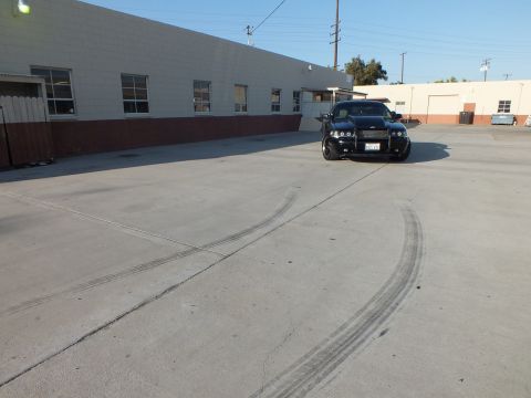 2003 Ford Crown Victoria - black sedan faces forward beside a warehouse, with looping tire skid marks fresh on the concrete lot.