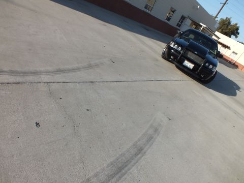 2003 Ford Crown Victoria - black sedan sits angled in a concrete lot with dark curving tire marks sweeping across the foreground pavement.