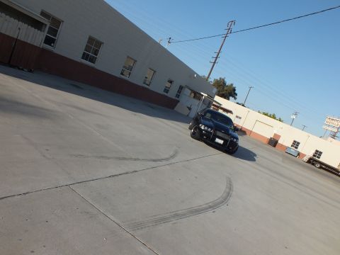 2003 Ford Crown Victoria - black sedan sits in a large concrete lot with looping tire skid marks curving across the pavement around it.