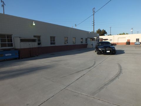 2003 Ford Crown Victoria - black sedan sits beside a warehouse as a long curved skid mark sweeps across the concrete lot in front of it.