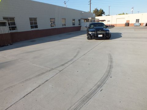 2003 Ford Crown Victoria - black sedan faces forward in a concrete lot with curving tire skid marks streaking across the pavement.