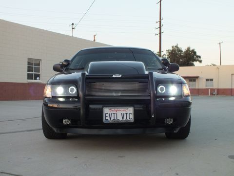 2003 Ford Crown Victoria - black Ford Crown Victoria with a brush guard and halo headlights sits in a lot showing its EVIL VIC California plate.