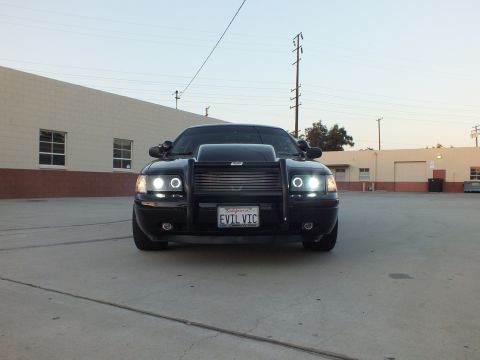 2003 Ford Crown Victoria - low front view of a black Ford Crown Victoria with push bar and lit halo headlights showing the EVIL VIC plate at dusk.