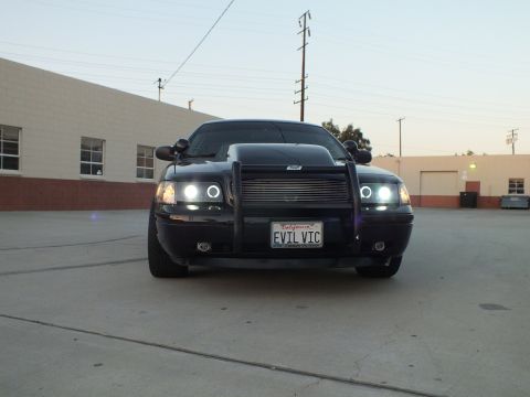 2003 Ford Crown Victoria - black Ford Crown Victoria with brush guard and halo headlights sits in a concrete lot displaying its EVIL VIC plate.