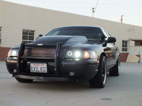 2003 Ford Crown Victoria - black Ford Crown Victoria with push bar and halo headlights sits at a front three-quarter angle in a sunlit lot.