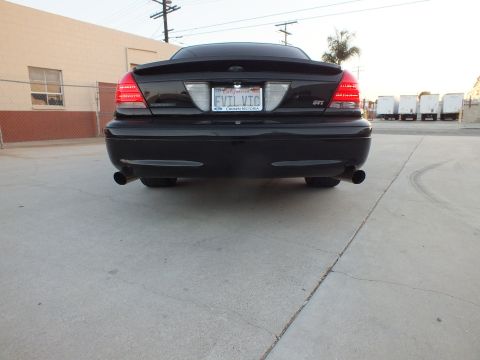 2003 Ford Crown Victoria - Low-angle rear view of a black full-size sedan with an EVIL VIC license plate parked in a paved lot.