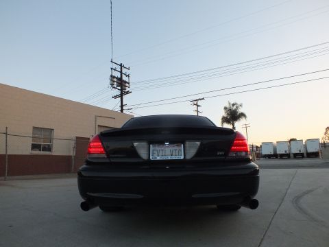 2003 Ford Crown Victoria - Rear view of a black full-size sedan with an EVIL VIC plate parked in a lot beside a tan building.