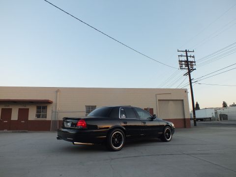 2003 Ford Crown Victoria - Rear three-quarter view of a lowered black full-size sedan parked in an industrial lot at dusk.