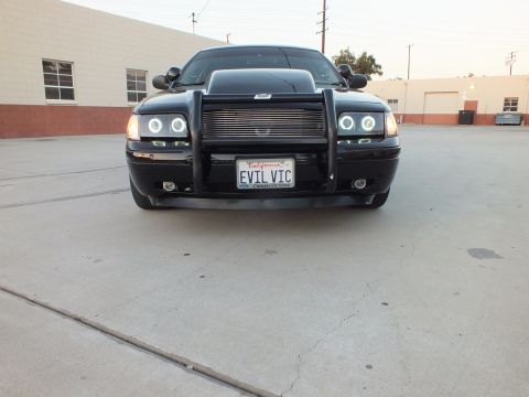2003 Ford Crown Victoria - Low head-on shot of a black sedan with a chrome brush guard, billet grille and halo headlights, plate EVIL VIC.