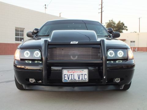 2003 Ford Crown Victoria - Head-on view of a black sedan with brush guard and halo headlights, EVIL VIC plate in a Crown Victoria frame.