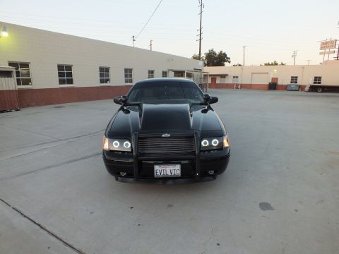 2003 Ford Crown Victoria - Front view of a black sedan with a raised hood scoop, brush guard and halo headlights in a paved lot.