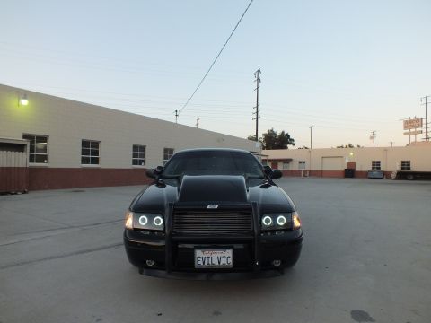 2003 Ford Crown Victoria - Head-on view of a black sedan with a hood scoop, brush guard, halo headlights and an EVIL VIC plate.