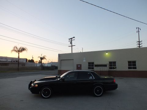 2003 Ford Crown Victoria - Driver-side profile of a lowered black full-size sedan on dark wheels parked in an industrial lot at dusk.