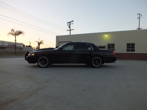 2003 Ford Crown Victoria - Side profile of a lowered black full-size sedan on dark wheels parked in a paved lot at dusk.