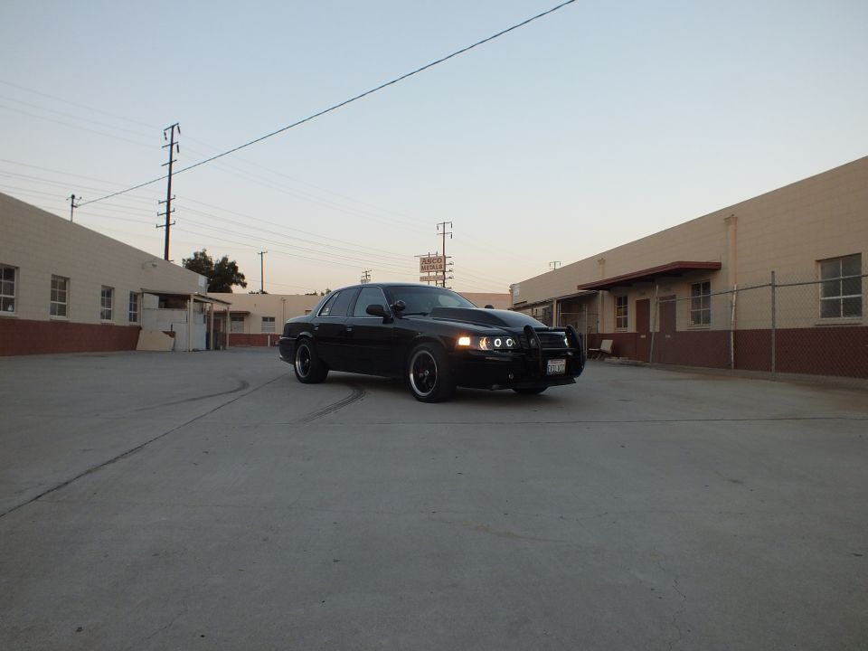 Black sedan with halo headlights parked in wide industrial lot at dusk