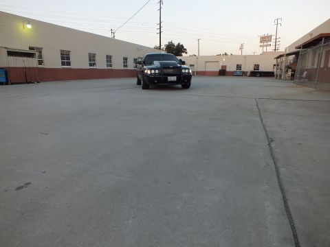 2003 Ford Crown Victoria - black sedan with halo headlights sits in the distance across an expansive concrete industrial lot at dusk.