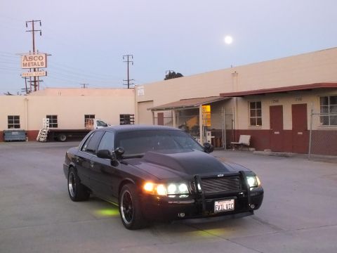 2003 Ford Crown Victoria - black Ford Crown Victoria with grille guard, lit headlights and green underglow near an ASCO Metals warehouse at dusk.