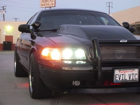 2003 Ford Crown Victoria - Close-up front quarter of a black Ford Crown Victoria with grille guard, glowing halo lights and California plate EVIL VIC.