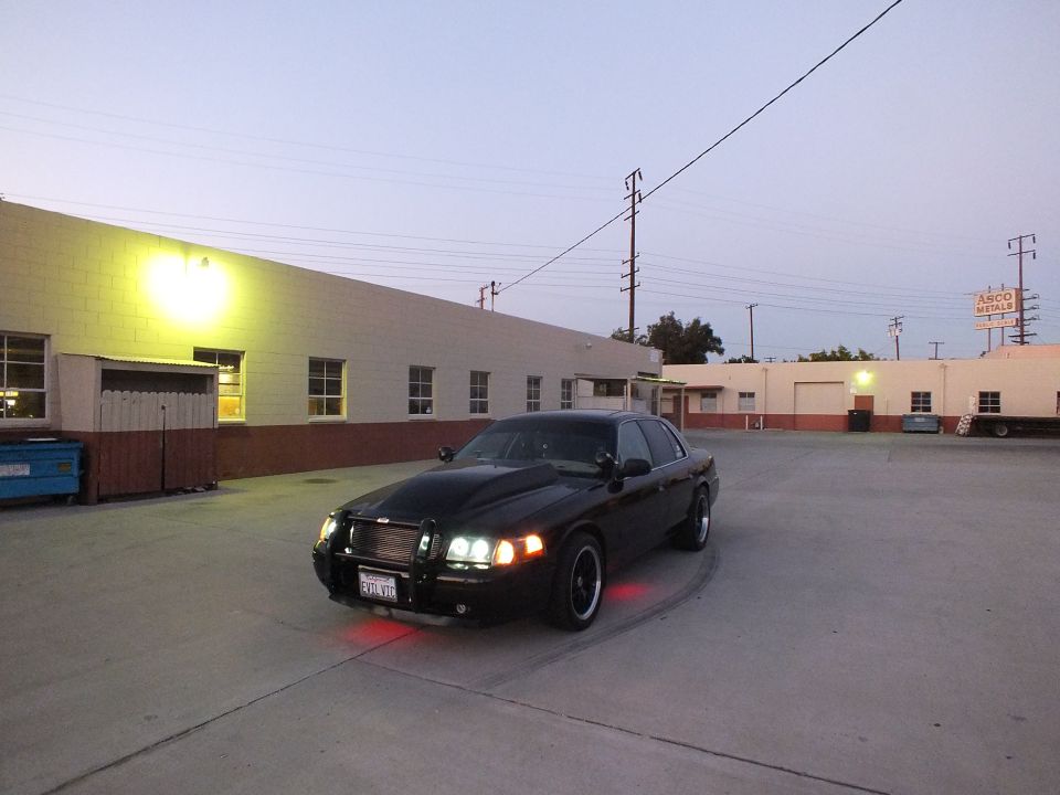 Black sedan with headlights and red underglow in industrial lot at dusk