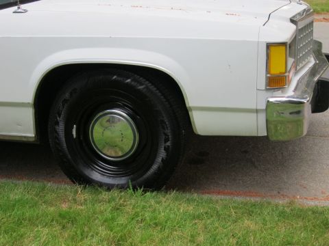 1991 Ford LTD Crown Victoria - Close-up of the front passenger side of a white 1991 Ford Crown Victoria LTD, showing the wheel and chrome bumper.