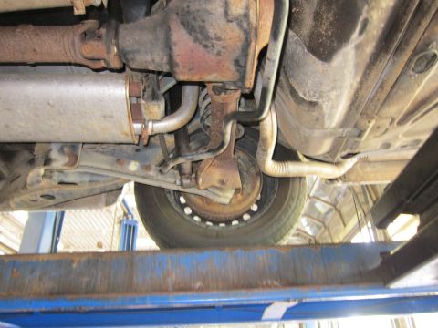 1991 Ford LTD Crown Victoria - The undercarriage of a vehicle is shown, revealing its exhaust system and suspension components while elevated on a lift.
