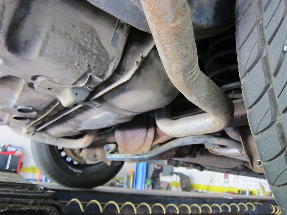 Undercarriage view of a vehicle, showing the exhaust system, differential, and tire. The vehicle is on a lift