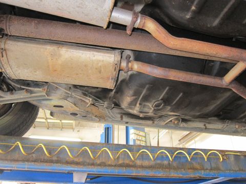 1991 Ford LTD Crown Victoria - Undercarriage view of a vehicle's exhaust pipes, muffler, and fuel tank, showing signs of age.