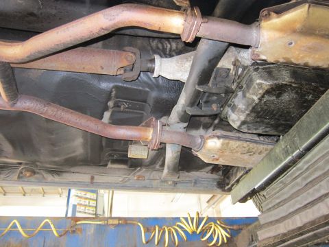 1991 Ford LTD Crown Victoria - The undercarriage of a vehicle is shown, with focus on the exhaust pipes, driveshaft, and transmission.