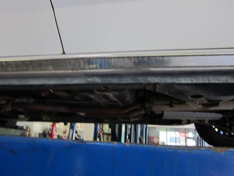 1991 Ford LTD Crown Victoria - The underside of a white car is visible, raised on a hydraulic lift for inspection.