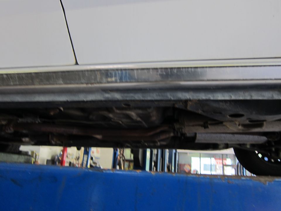 Underside of a white car on a lift, showing exhaust and suspension components