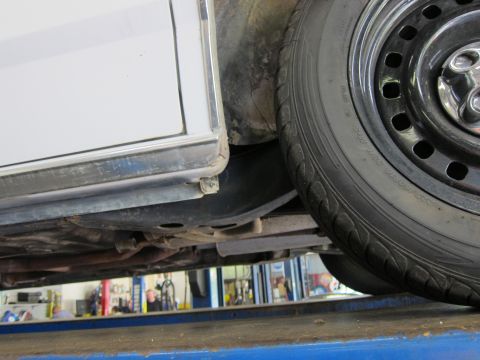 1991 Ford LTD Crown Victoria - Close-up view of the undercarriage and wheel well of a white vehicle, possibly in a repair shop.