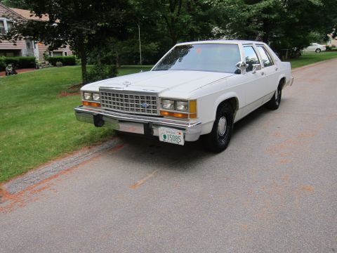 1991 Ford LTD Crown Victoria - A white sedan, likely a 1987 model, is parked on a residential street.