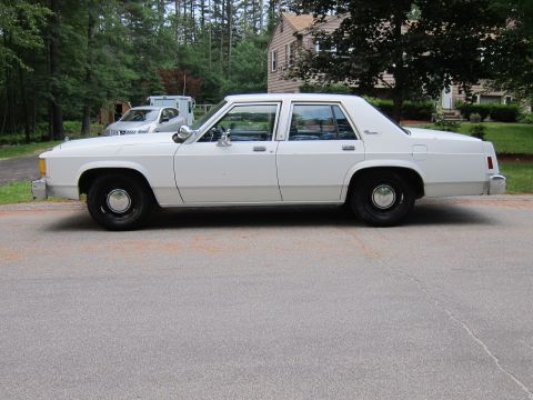 1991 Ford LTD Crown Victoria - This white sedan, likely a 1988 Ford LTD Crown Victoria, is shown from the side. The vehicle has a classic boxy sedan profile.