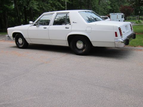 1991 Ford LTD Crown Victoria - A white sedan is parked on a paved surface with trees in the background.