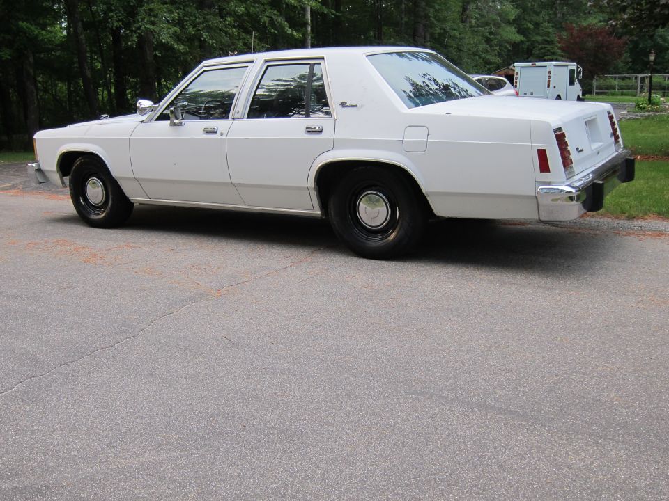 White sedan parked on asphalt, trees in background