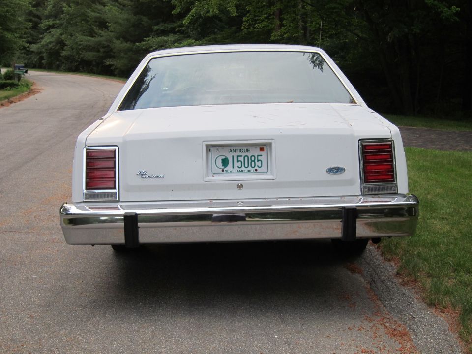 White sedan's rear end with chrome bumper and horizontal taillights. New Hampshire antique license plate 15085