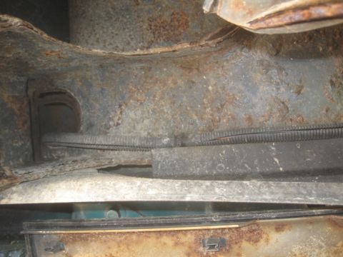1993 Ford Bronco - The heavily rusted undercarriage of a vehicle shows a wiring harness and structural components.
