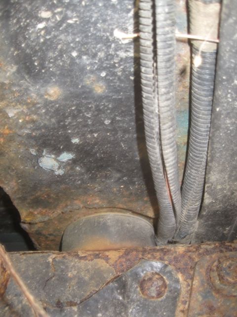 1993 Ford Bronco - This image shows the heavily rusted undercarriage of a vehicle, with electrical conduits and a suspension bushing visible.