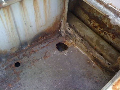 1964 Ford Ranchero - The corner of a metal structure shows significant rust and a hole, indicating decay.