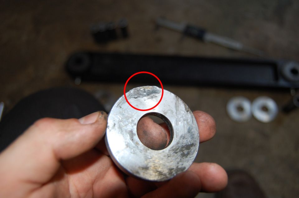 Hand holding a circular metal part with a hole, showing wear and damage