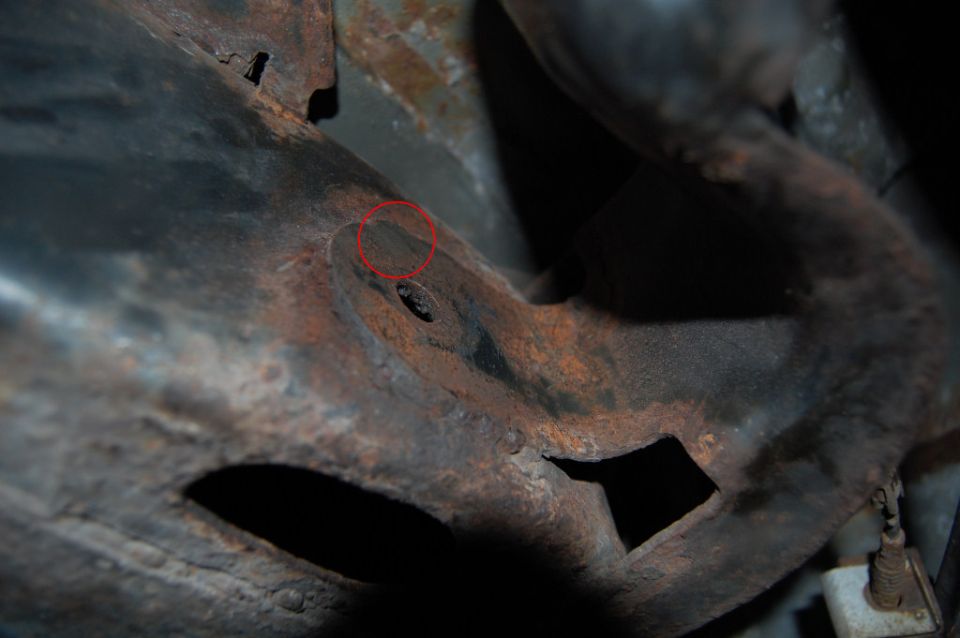 Rusted metal frame of a vehicle, showing corrosion and a red circle around a bolt hole