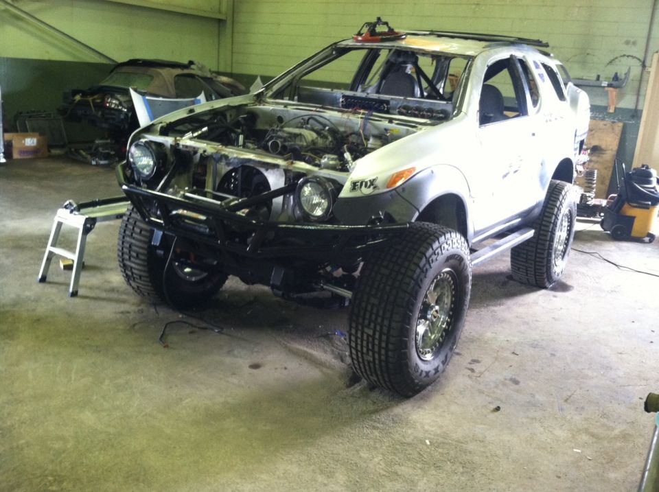 White SUV with custom bumper and off-road tires, hood open, in a workshop