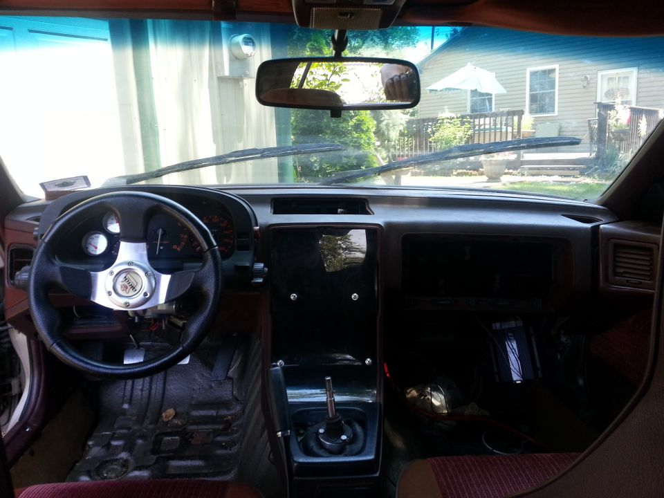 1987 Mazda RX-7 interior with aftermarket steering wheel, manual shifter, and worn floor mats