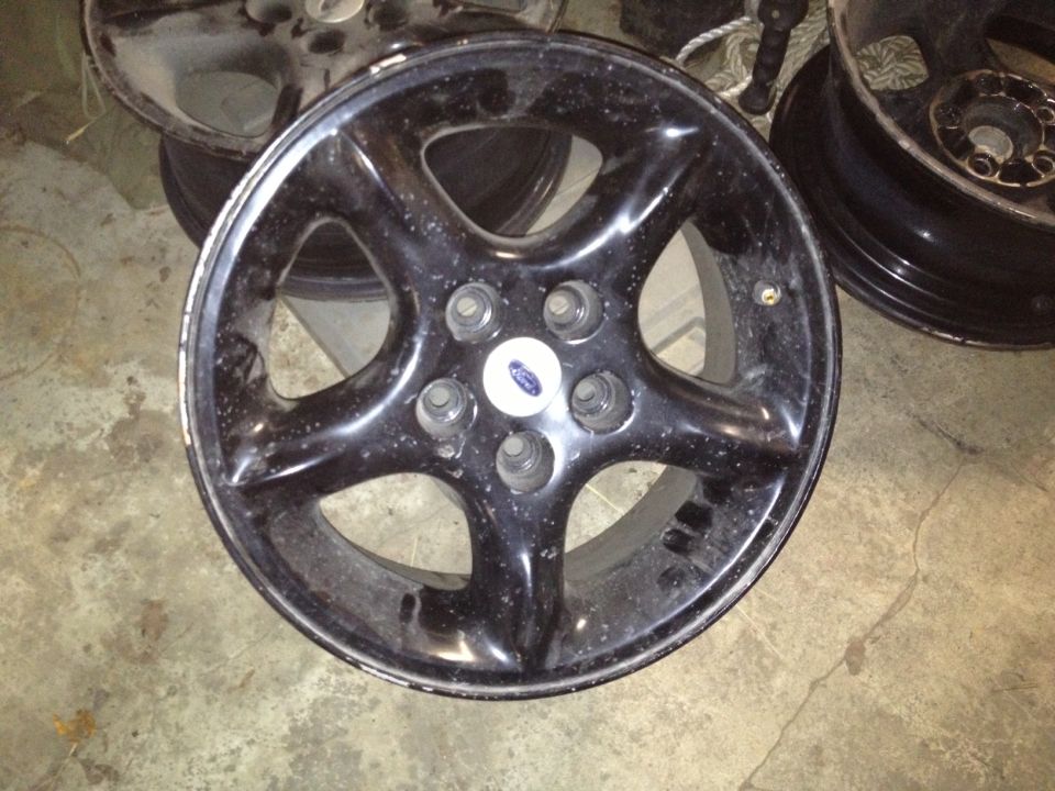 Black five-spoke wheel with a Ford logo in the center. Other wheels are visible in the background