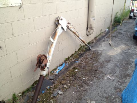 2000 Ford E350 - A weathered crane arm and winch are positioned against a building wall, with debris on the ground.
