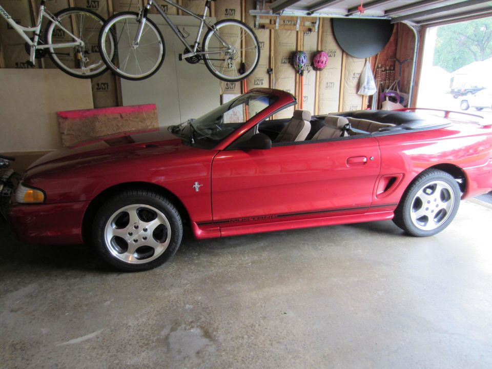 Red 1995 Ford Mustang convertible side view. "Mustang" text visible on rocker panel